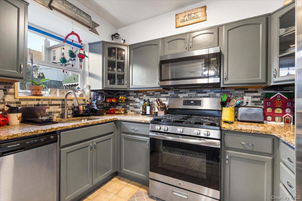 2761 Hering Avenue Bronx, NY 10469 - Photo 11 of 29 Kitchen with gray cabinetry, glass insert cabinets, stainless steel appliances, and light stone countertops