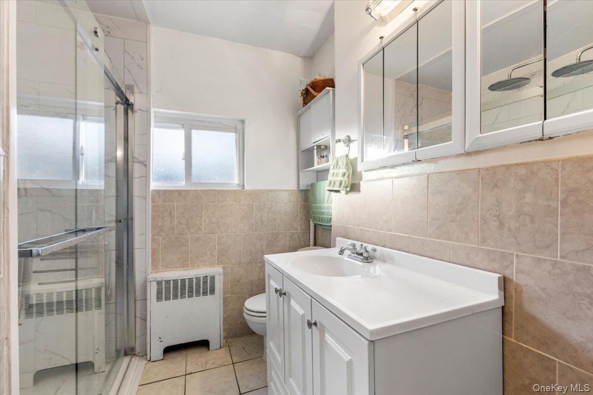 2761 Hering Avenue Bronx, NY 10469 - Photo 18 of 29 Bathroom featuring radiator heating unit, vanity, a shower stall, tile walls, and light tile patterned flooring