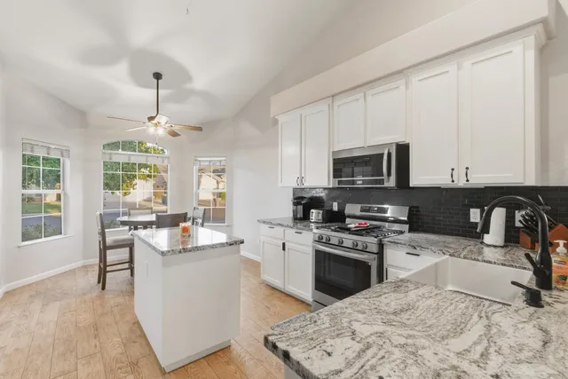 a view of a livingroom with a kitchen island a fireplace a ceiling fan and wooden floor