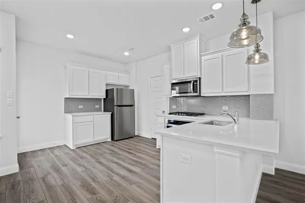 a kitchen with stainless steel appliances granite countertop a refrigerator oven a sink dishwasher and white cabinets with wooden floor