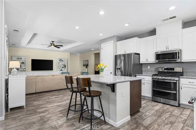 a kitchen with kitchen island stainless steel appliances a stove a sink a microwave a refrigerator a stove a microwave oven with white cabinets and couches