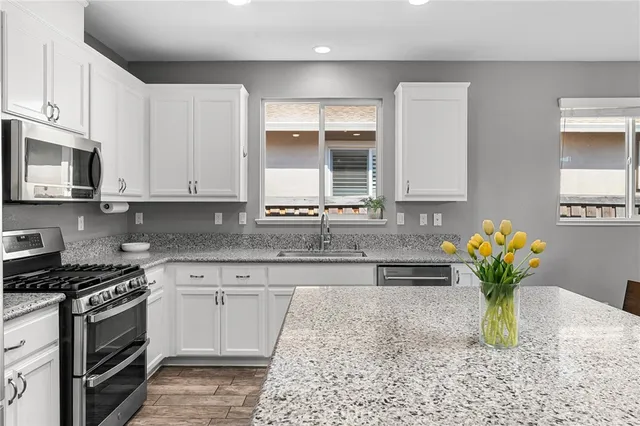 a white kitchen with stainless steel appliances granite countertop a sink a stove and a granite counter tops