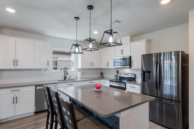 a kitchen with stainless steel appliances kitchen island granite countertop a dining table chairs refrigerator and sink