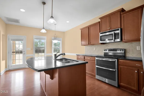 a kitchen with stainless steel appliances granite countertop a stove a sink dishwasher a refrigerator and a microwave oven with wooden floor