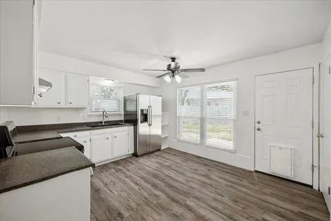 a kitchen with granite countertop a stove a sink and white cabinets with wooden floor