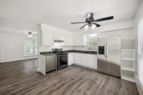 a kitchen with granite countertop a refrigerator a sink dishwasher a stove and white cabinets with wooden floor