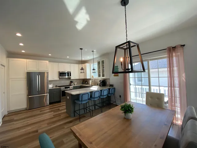 a kitchen with stainless steel appliances granite countertop a refrigerator a stove a sink dishwasher and a dining table with wooden floor