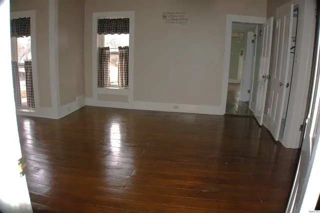 a view of an empty room with wooden floor and a window