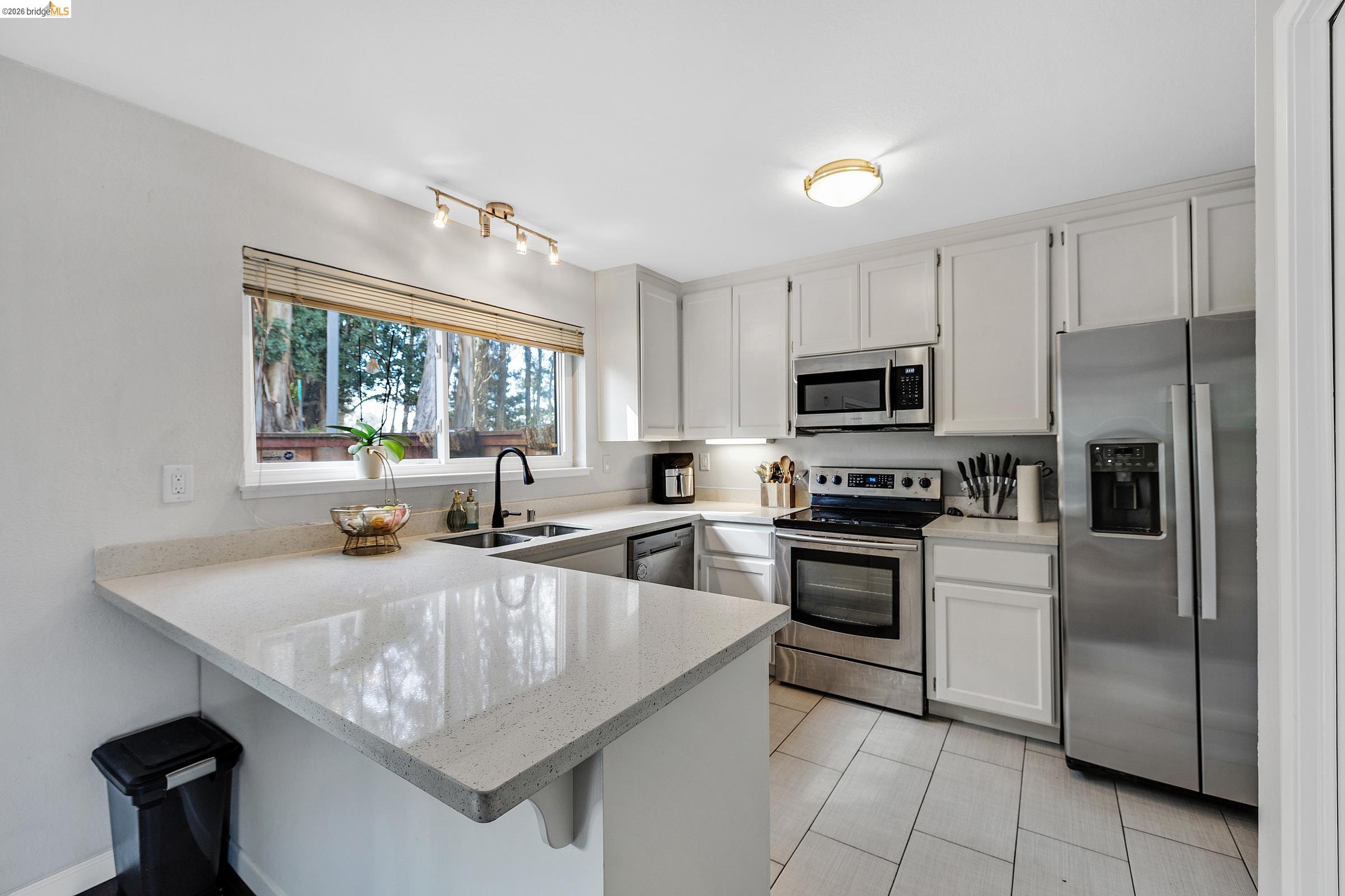 407 Vista Heights Road El Cerrito, CA 94530 - Photo 5 of 29 Kitchen featuring stainless steel appliances, a kitchen bar, a peninsula, light stone countertops, and white cabinetry