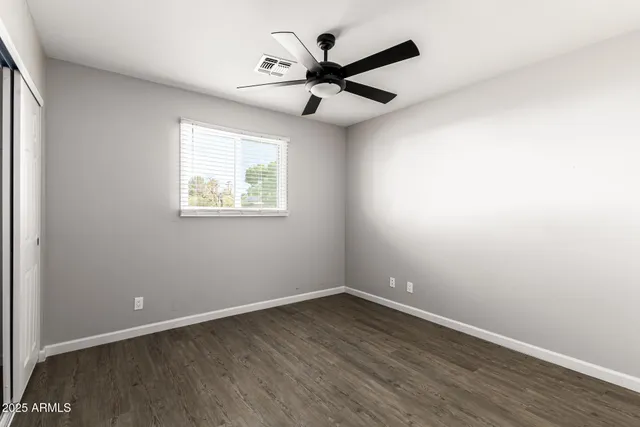 an empty room with wooden floor ceiling fan and windows