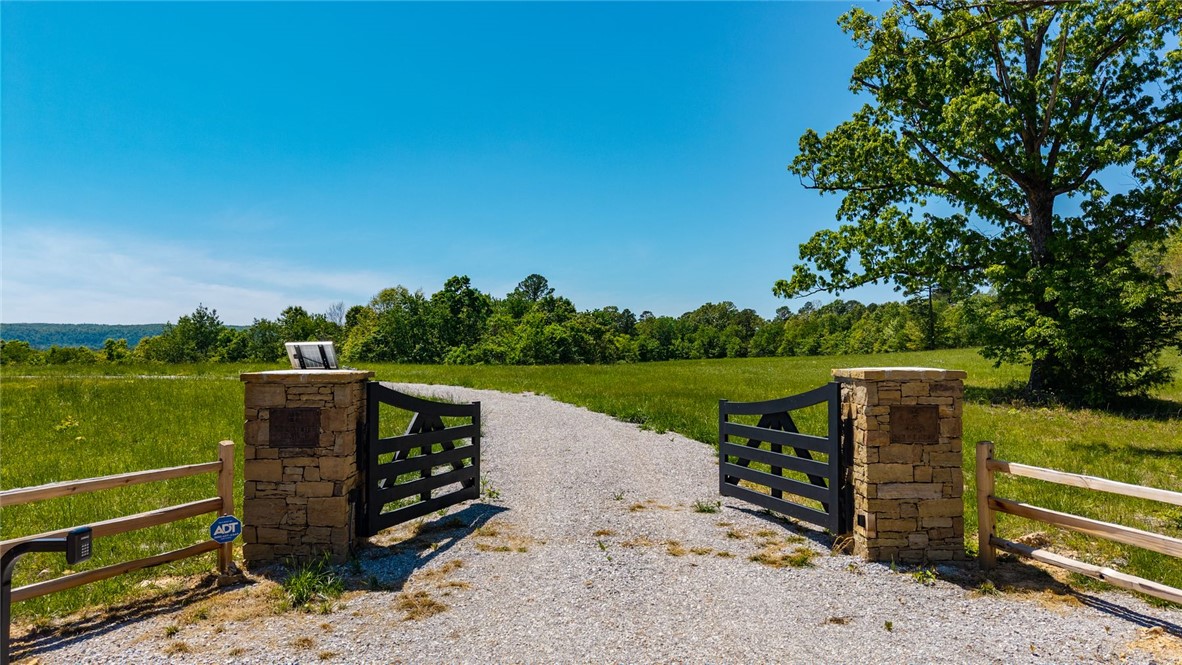 425 Barnhardt Road Timbo, AR 72680 - Photo 3 of 60 Gravel driveway entrance featuring stone pillars and a dark wood gate, bordered by a split-rail fence and expansive green fields