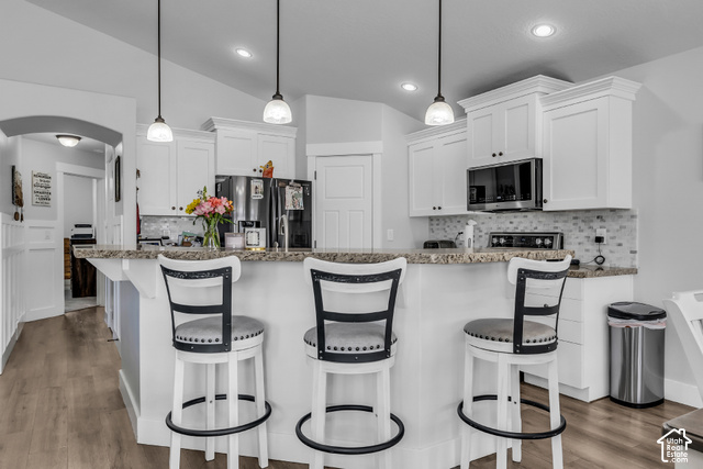 12992 West Geronimo Road Riverton, UT 84096 - Photo 7 of 25 Kitchen featuring white cabinetry with crown molding, a mosaic tile backsplash, stainless steel appliances, and a breakfast bar with stone-finish countertops