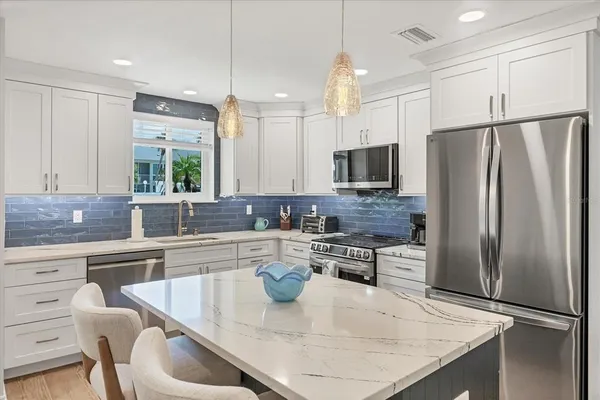 a kitchen with stainless steel appliances granite countertop a refrigerator a sink a stove a dining table and chairs