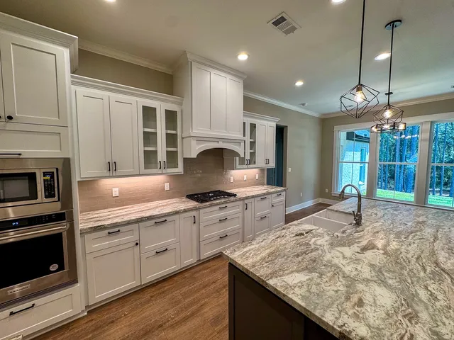a kitchen with stainless steel appliances granite countertop sink stove and white cabinets with wooden floor