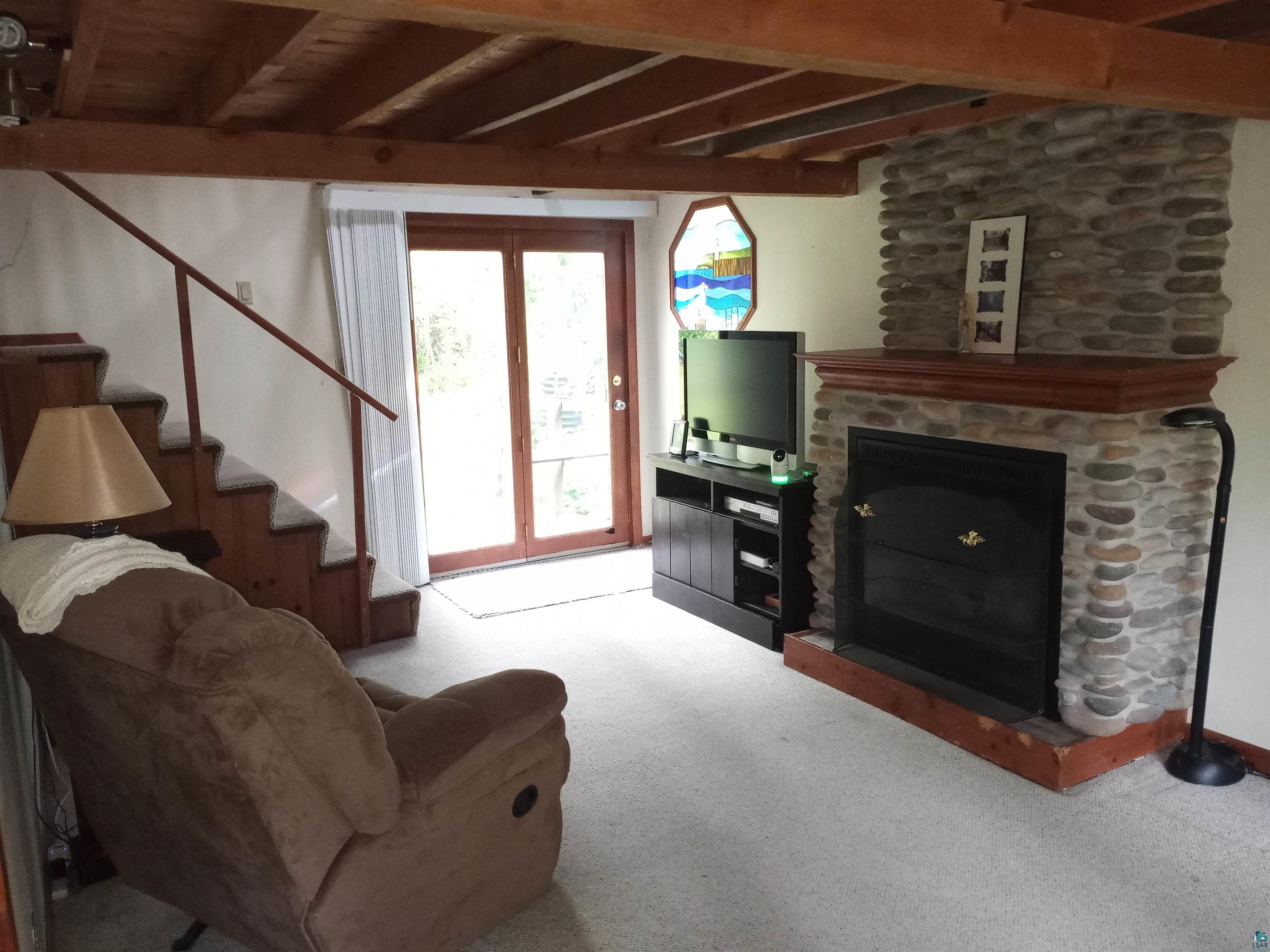 22715 Elm Street Cornucopia, WI 54827 - Photo 7 of 23 Carpeted living area with stairs, a fireplace, and beam ceiling