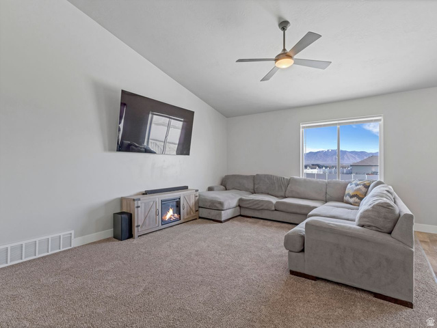 573 South Maxwell Drive Grantsville, UT 84029 - Photo 4 of 25 Living area with lofted ceiling, plenty of natural light, a glass covered fireplace, ceiling fan, and carpet