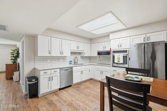 a kitchen with stainless steel appliances a stove a sink dishwasher a refrigerator and white cabinets with wooden floor