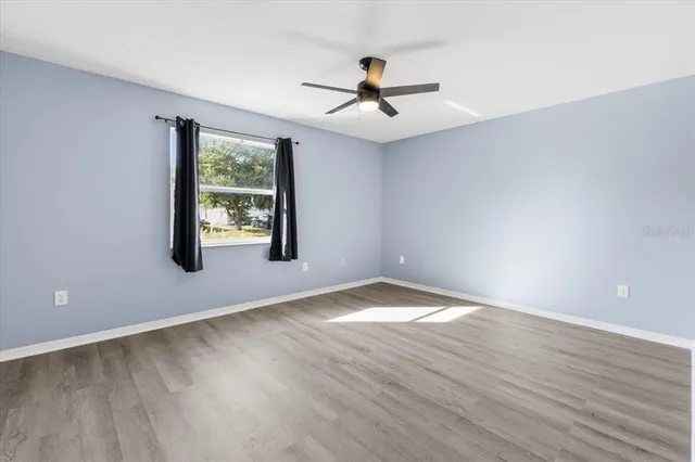 an empty room with wooden floor fan and windows