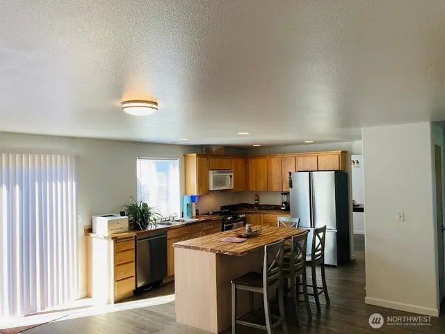 a kitchen with stainless steel appliances granite countertop a stove a refrigerator a sink a dining table and chairs