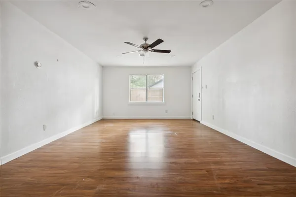 an empty room with wooden floor chandelier fan and windows