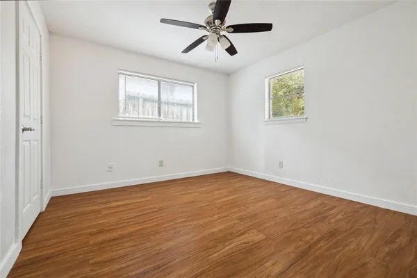 an empty room with wooden floor ceiling fan and windows