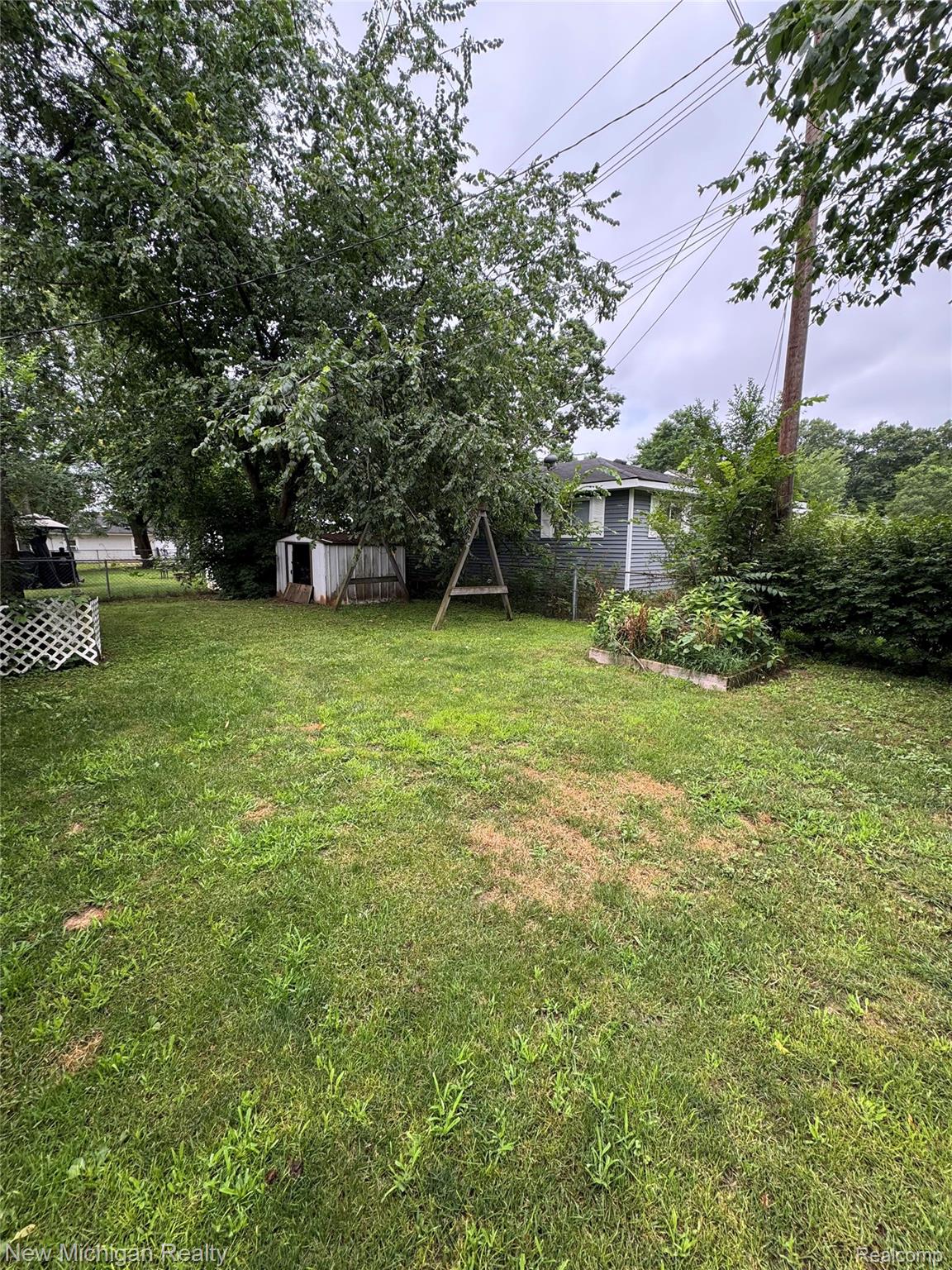 870 Farnsworth Road White Lake, MI 48386 - Photo 4 of 20 Expansive green space featuring a garden bed, mature trees, and a storage shed