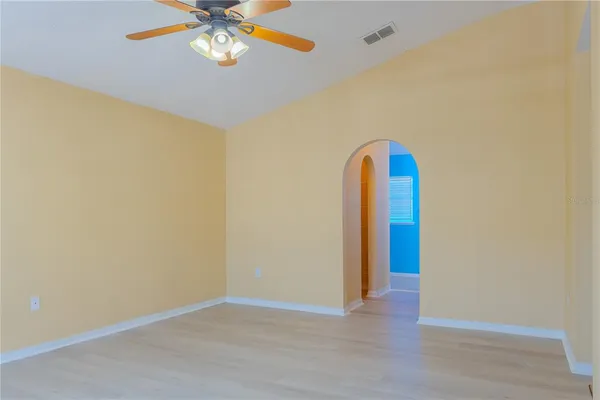 a view of an empty room with wooden floor and a ceiling fan