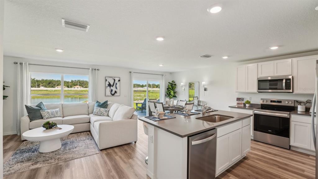 9806 Southeast 161st Lane Road Summerfield, FL 34491 - Photo 6 of 29 a kitchen with a stove a sink a kitchen island with a couches and wooden floor