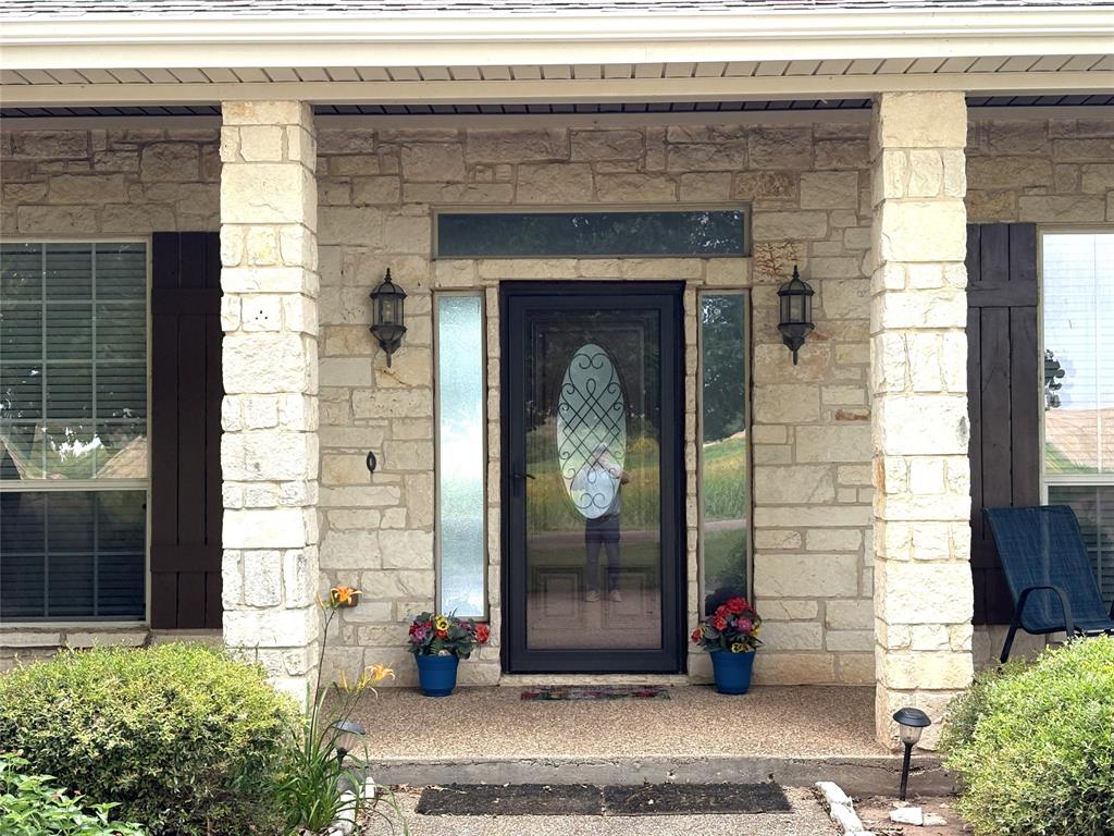 1170 Brazos Loop Gholson, TX 76705 - Photo 7 of 37 Stone facade entrance featuring a decorative glass storm door, flanking sidelights, and an overhead transom window