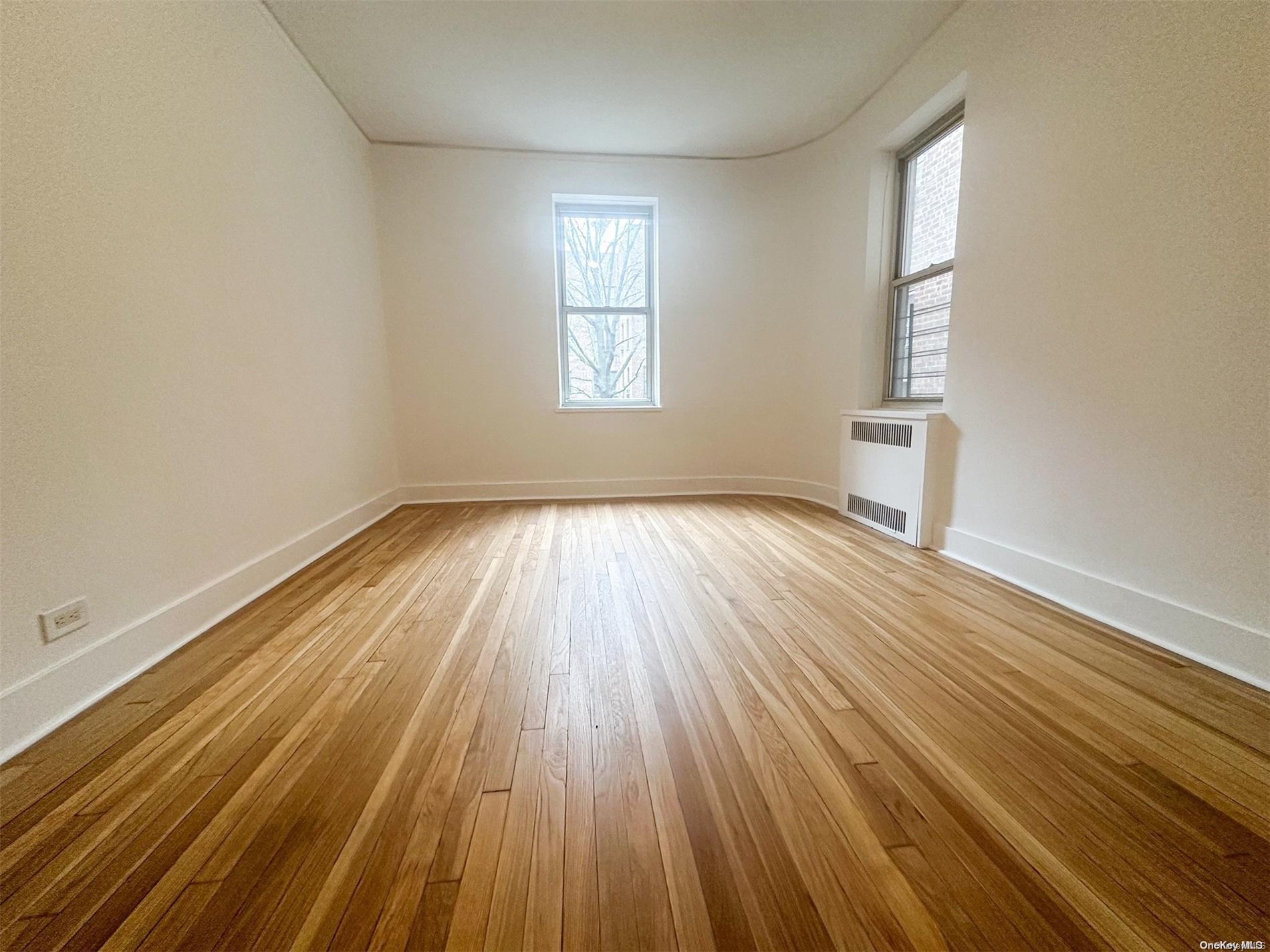 110-34 73rd Road, Unit 4C Queens, NY 11375 - Photo 7 of 10 an empty room with wooden floor and windows