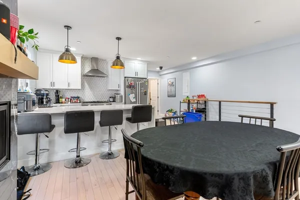 a kitchen with stainless steel appliances kitchen island granite countertop a dining table chairs and a refrigerator