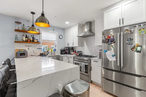 a kitchen with stainless steel appliances a refrigerator a sink dishwasher a oven a dining table and chairs with wooden floor