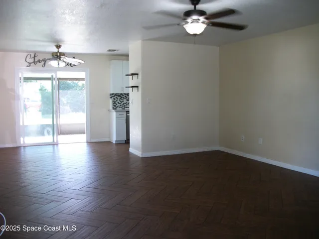 an empty room with wooden floor chandelier fan and windows