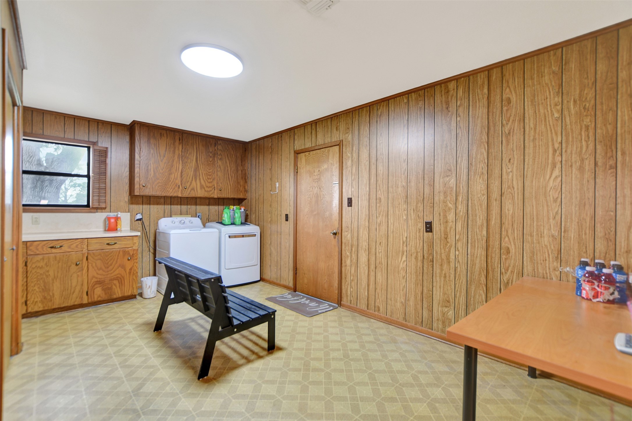 341 South S Loop Bellville, TX 77418 - Photo 17 of 33 This room features wood-paneled walls, a washer and dryer, cabinetry, and a small window for natural light. It also includes a bench and table, offering a versatile space for laundry and storage needs.