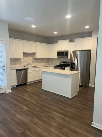 a kitchen with kitchen island a sink a stove a refrigerator and white cabinets with wooden floor