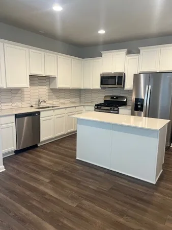 a kitchen with stainless steel appliances granite countertop a stove top oven a sink a refrigerator white cabinets and wooden floor