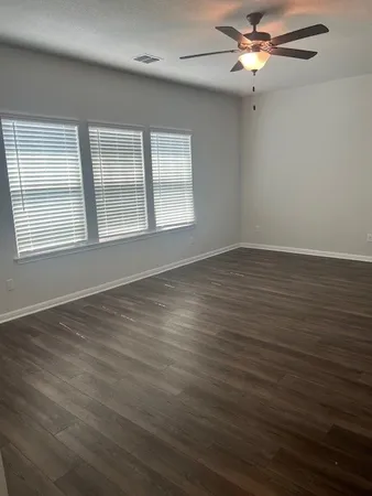 an empty room with wooden floor fan and windows