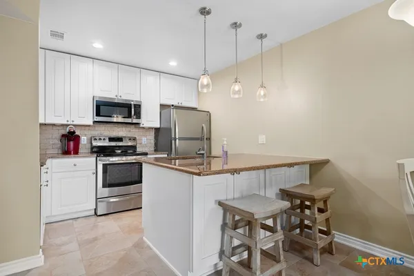 a kitchen with stainless steel appliances kitchen island a refrigerator a stove a sink a dining table and chairs