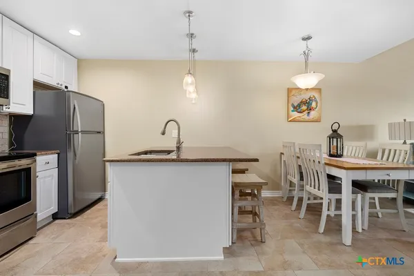 a kitchen with stainless steel appliances granite countertop a sink a stove a refrigerator a dining table and chairs