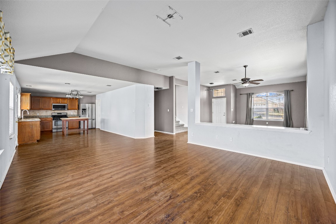 1321 Bunratty Circle Pflugerville, TX 78660 - Photo 14 of 31 Unfurnished living room featuring dark wood-style floors, stairway, ceiling fan, a chandelier, and vaulted ceiling
