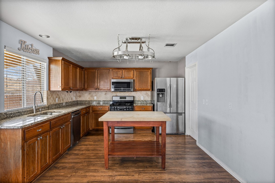 1321 Bunratty Circle Pflugerville, TX 78660 - Photo 15 of 31 Kitchen featuring brown cabinets, appliances with stainless steel finishes, dark stone countertops, and dark wood-type flooring