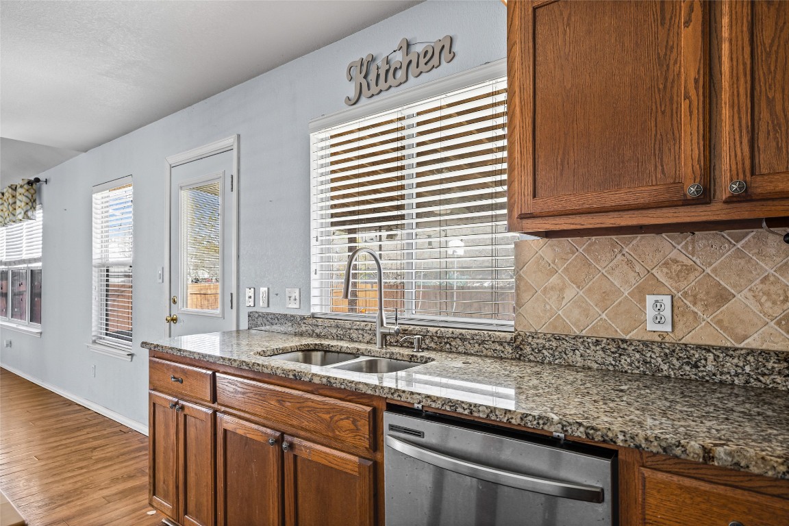 1321 Bunratty Circle Pflugerville, TX 78660 - Photo 17 of 31 Kitchen featuring dark stone counters, dishwasher, brown cabinets, and backsplash