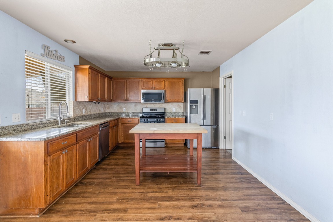 1321 Bunratty Circle Pflugerville, TX 78660 - Photo 7 of 31 Kitchen featuring brown cabinetry, appliances with stainless steel finishes, dark wood finished floors, and light stone counters