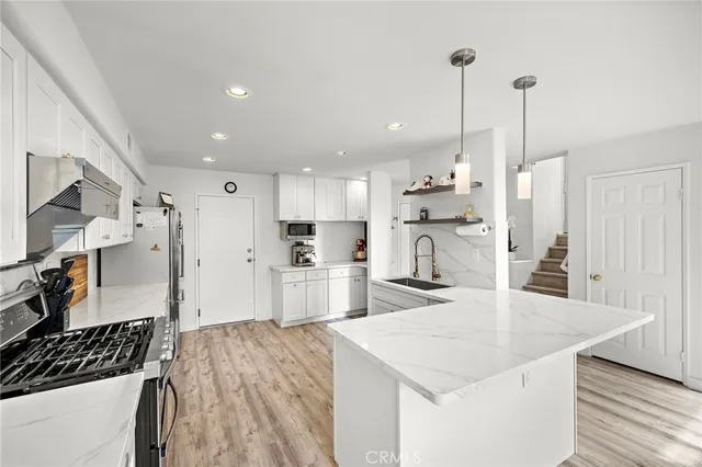 a kitchen with stainless steel appliances kitchen island granite countertop a refrigerator a sink dishwasher and white cabinets with wooden floor