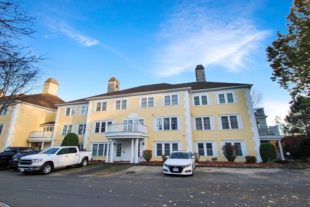 a front view of a building with lot of cars and trees