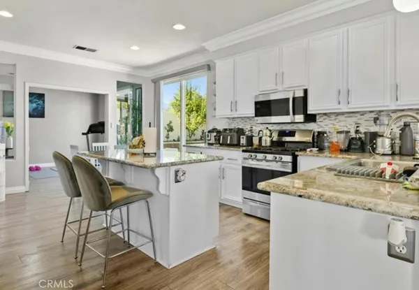 a kitchen with stainless steel appliances granite countertop a stove a sink a microwave a refrigerator white cabinets and a dining table with wooden floor
