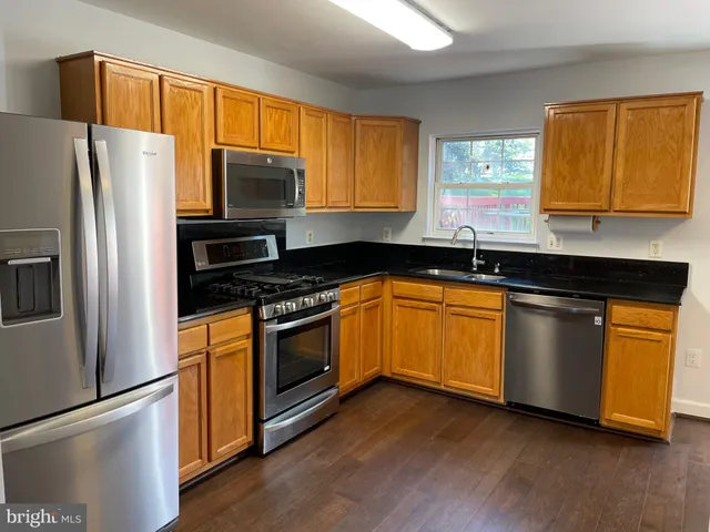 a kitchen with granite countertop wooden floors stainless steel appliances and sink