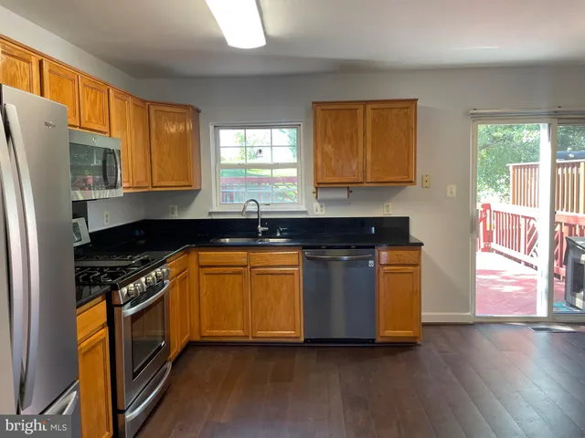 a kitchen with granite countertop wooden floors stainless steel appliances a sink and a window