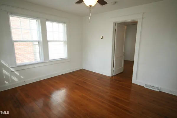 an empty room with wooden floor chandelier fan and windows