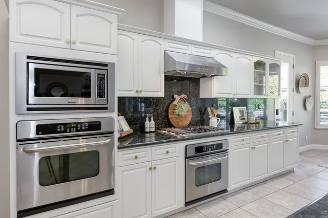 a kitchen with stainless steel appliances granite countertop white cabinets and a stove top oven
